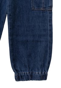 Pantalones de mezclilla azul oscuro con puños elásticos y un bolsillo lateral. La textura desgastada realza el aspecto general de la tela.