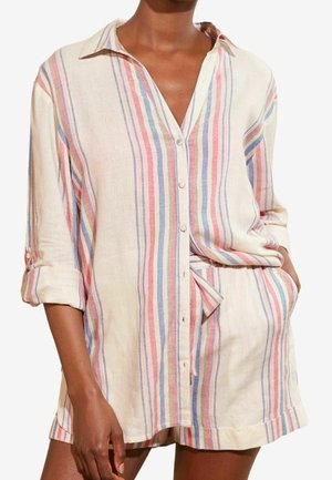 Vrouw draagt een loszittend, button-down, shirt met lange mouwen en bijpassende short met verticale pastelkleurige strepen in blauw, roze en wit.