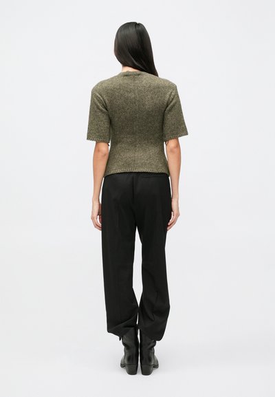 Olivovo zelený pletený top s krátkymi rukávmi, priliehavým strihom a dĺžkou ku pásu, nosený s voľnými čiernymi nohavicami a čiernymi členkovými čižmami.