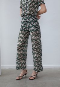 Green and beige patterned co-ord set featuring a short-sleeve top and wide-leg trousers with a circular design, complemented by black strappy heels.