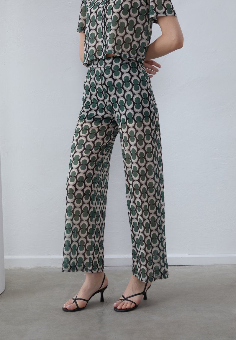 Green and beige patterned co-ord set featuring a short-sleeve top and wide-leg trousers with a circular design, complemented by black strappy heels.