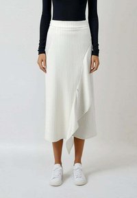 Jupe midi blanche à nervures avec un ourlet asymétrique, présentant une texture lisse et une taille confortable, associée à des baskets blanches.