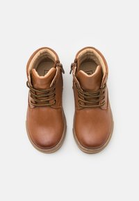 Bruine leren enkelboots met decoratieve veters en zijritsen. Ronde neus en gevoerde binnenkant. Geprofileerde rubberen zool voor grip.