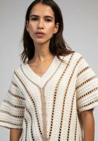 Pull en tricot crème avec un col en V, présentant des rayures verticales et horizontales, une texture à mailles ouvertes et des manches courtes.