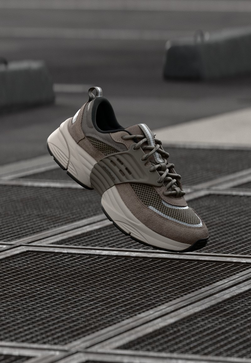 Braune Mesh- und Wildledersneaker mit einer dicken weißen Sohle, ausgestattet mit einer gepolsterten Zunge, Schnürsystem und reflektierenden Akzenten.