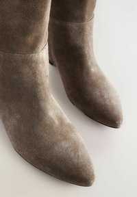 Brown suede ankle boots with a pointed toe and minimal stitching details. The texture is soft with a slight sheen, on a dark sole.