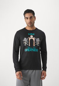 Black long-sleeve t-shirt made of cotton, featuring a graphic design with lions and an arch. Text reads "Strive For Greatness" in turquoise.