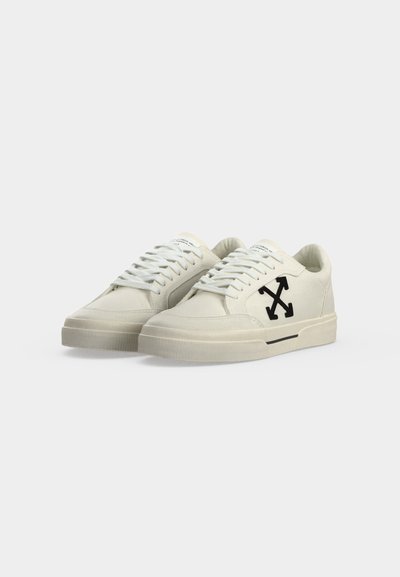 Χαμηλά sneakers εκρού με κορδόνια, παχιά σόλα και μαύρο σταυρωτό λογότυπο βέλους στο πλάι.