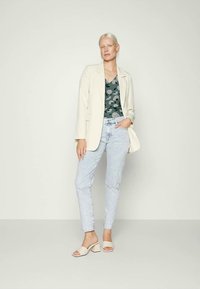 Blazer bege claro, blusa floral verde escuro, jeans azul claro e saltos em creme. Tecido suave, corte ajustado e padrões subtis.