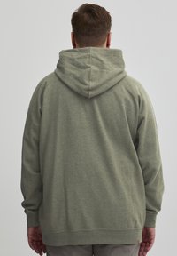 Sudadera con capucha en verde claro, hecha de un tejido suave. Presenta un bolsillo tipo canguro y puños acanalados, con un corte relajado y detalles de costura.