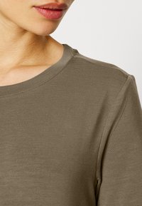 Camisola de manga longa em verde oliva, com decote redondo e detalhes de costura subtil. O tecido parece suave, com um design ajustado.