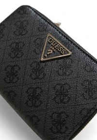 Portafoglio Guess nero con motivo a logo in rilievo, hardware triangolare dorato e materiale sintetico testurizzato. Chiusura con zip visibile.