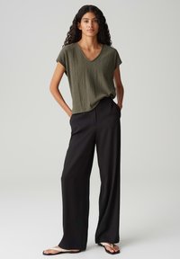 Olive green, short-sleeve, textured V-neck top paired with black, loose-fitting trousers and black flip-flops. Simple, clean design.