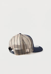 Tumedat sinine baasipalli kork, millel on kõver rõngas, võrkkangast tagumine osa ja beežid vertikaalsed triibud. Reguleeritav rihm. Lame õmblemise detail.