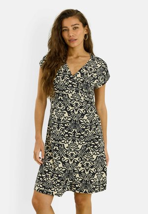 Mujer con cabello largo y ondulado que lleva pendientes de aro y un vestido de manga corta con escote en V y estampado floral en blanco y negro.