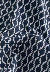 Tessuto blu navy con un motivo a zigzag bianco, caratterizzato da una texture liscia e un aspetto drappeggiato. Il design è geometrico e ripetitivo.