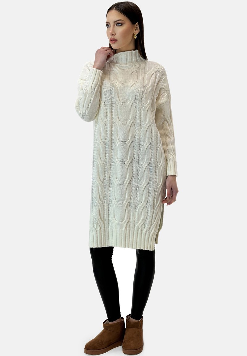 Cable-knit turtleneck kjole i creme, med ribbede manchetter og kant, parret med sorte leggings og brune ankelstøvler.