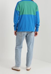 Långärmad skjorta i blå och grön färgblockering med avslappnad passform, kombinerad med ljusblå jeans och vita sneakers. Slät textur.