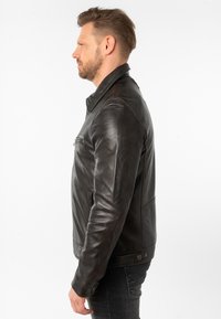 Zwarte leren jas met een slim fit, opstaande kraag en ritsvakken aan de voorkant. Zachte textuur en minimalistisch ontwerp.