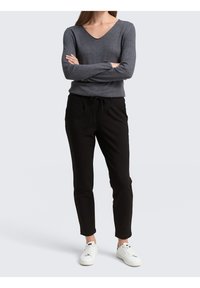 Maglione grigio a maniche lunghe con scollo a V, abbinato a pantaloni neri con coulisse e sneaker bianche. Un outfit semplice e casual.