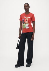 Raudona marškinėliai su Kalėdų tema, kuriuose pavaizduoti elniai ir šventiniai raidžių užrašai, skaitantys "MEILĖ". Derinami su juodomis plačiomis kelnėmis.