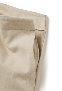 Tissu beige plié pour montrer une fermeture éclair dissimulée le long de la couture sur un fond blanc uni.