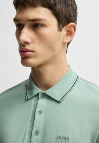 Mint green polo shirt in textured fabric, featuring a black-trimmed collar, two-button placket, and embroidered "BOSS" logo on the chest.