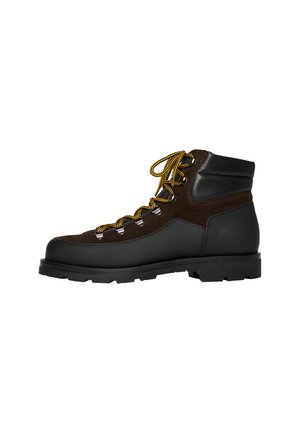 Botas de senderismo marrones y negras con una suela de goma resistente, ojetes metálicos y cordones amarillos. La parte superior combina cuero liso y gamuza texturizada.