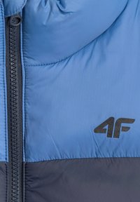 Section de veste matelassée bleu et gris foncé avec fermeture éclair noire et logo noir "4F" sur la poitrine.