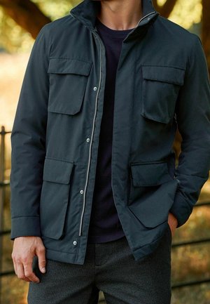 Černá lehká bunda se zapínáním na zip vpředu, vysokým límcem, dvěma velkými kapsami na hrudi a dvěma bočními kapsami. Hladká textura, neformální design.