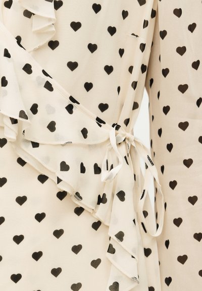 Ύφασμα κρεμ με μαύρο σχέδιο καρδιάς, διαθέτει στρωματοποιημένες βολάν και δεμένη κορδέλα στη μέση.