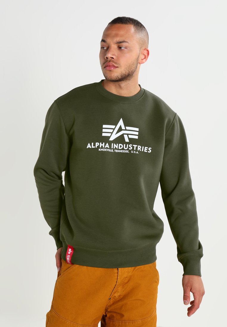 Felpa verde oliva con collo rotondo, caratterizzata da un grande logo bianco "Alpha Industries" sul davanti e un'etichetta rossa sull'orlo.