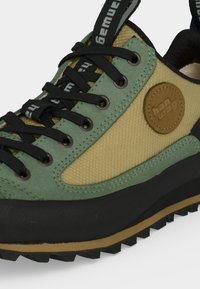 Πράσινο και μπεζ πεζοπορικό παπούτσι με μαύρα κορδόνια, μαύρη σόλα και στρογγυλό καφέ σήμα λογότυπου στο πλευρικό πάνελ.