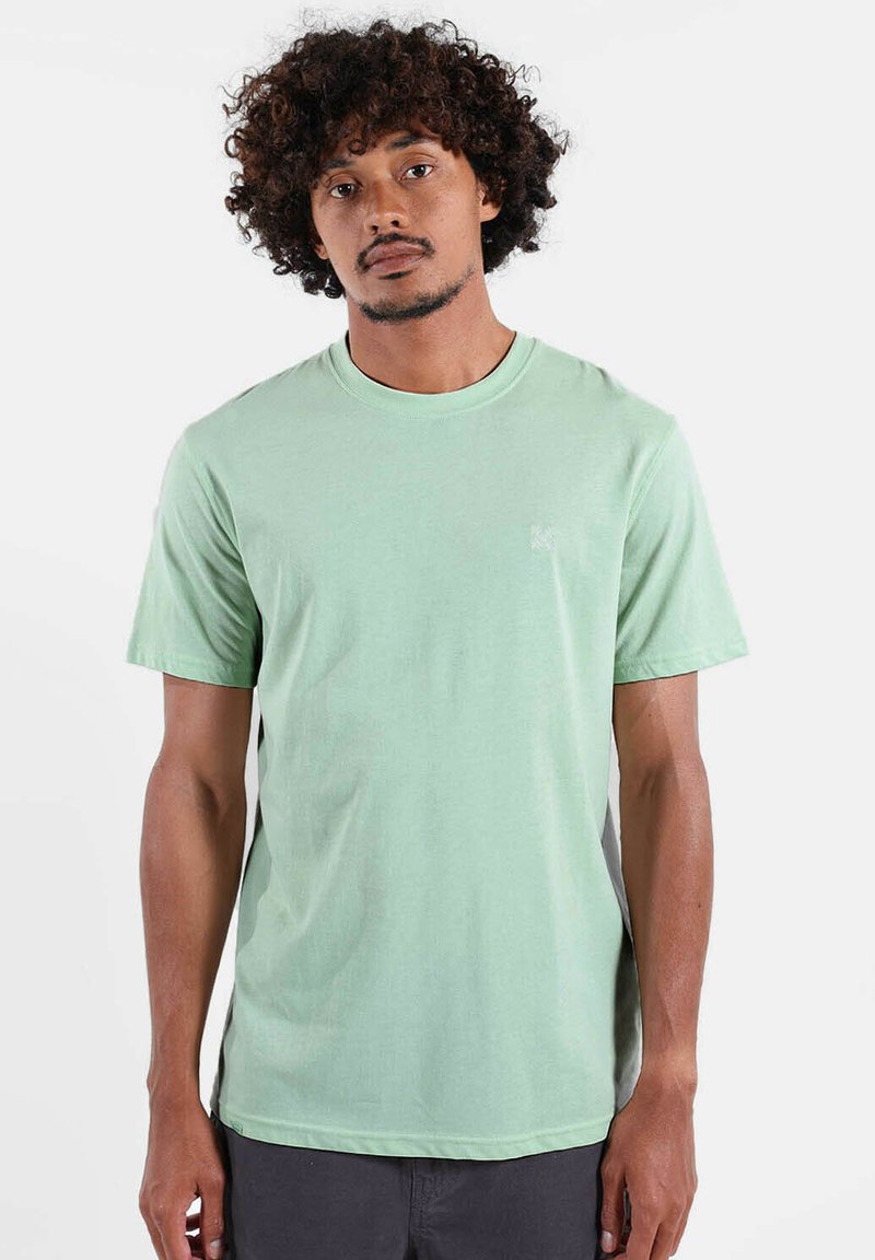 T-shirt en coton vert menthe avec un col rond et des manches courtes. Présente un petit logo sur le côté gauche de la poitrine et une texture lisse.