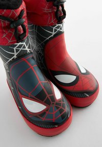 Bottes en caoutchouc rouges et noires avec des graphiques de Spider-Man, des motifs de toile texturés et de grands designs d'yeux de personnage sur la zone des orteils.