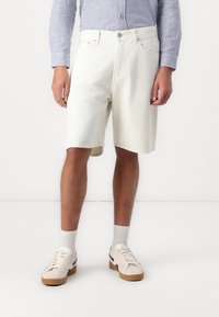 Hvide denimshorts med en afslappet pasform, der har forlommer og knaplukning, parret med lyse sneakers og ankelsokker.