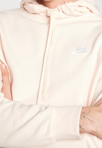 Ljusrosa Nike hoodie med dragsko i huvan, med en vit Nike-logotyp på bröstet och ribbade muddar på ärmarna. Mjuk tygkvalitet.