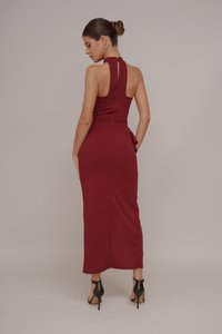Form-fitting burgundy dress with a high neck, open back, and ruffle detail at the waist, paired with black high-heeled shoes.