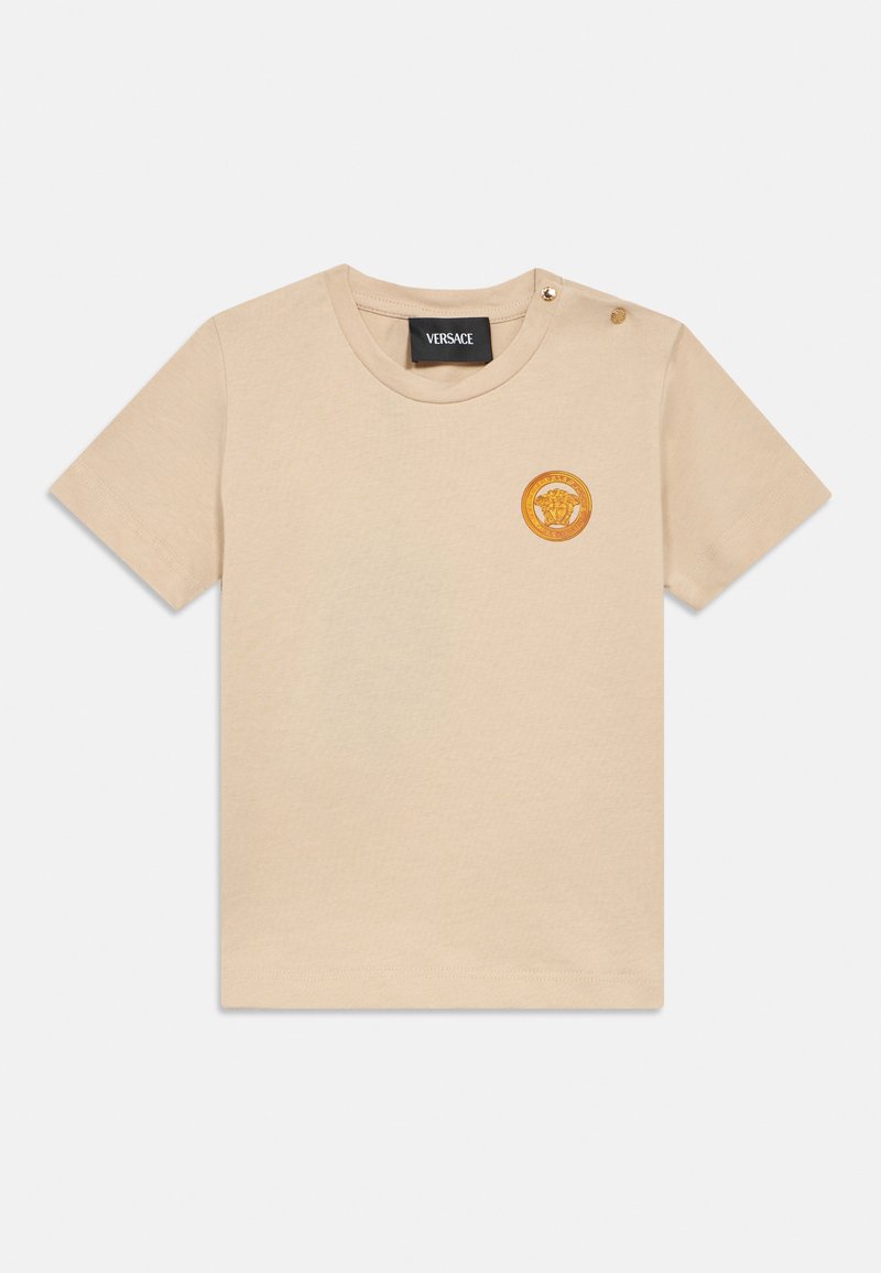 Μπεζ βαμβακερό t-shirt με κοντά μανίκια, με στρογγυλή λαιμαριά και χρυσό κυκλικό λογότυπο στο αριστερό στήθος, με λεπτομέρεια κουμπιού snap στον ώμο.