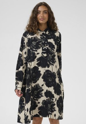 Rochie florală cu flori mari negre pe un fundal bej, mâneci lungi, deschidere cu butoane în față și croială lejeră.