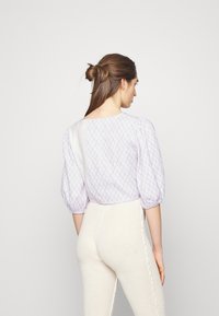 Blusa de algodão lilás claro com mangas bufantes e padrão de diamantes, combinada com calças creme de malha ribada com detalhe de costura lateral.