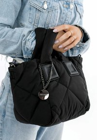 Borsa a tracolla nera trapuntata con texture imbottita, manici in due tessuti, dettagli in pelle e una catena metallica con un'etichetta circolare.