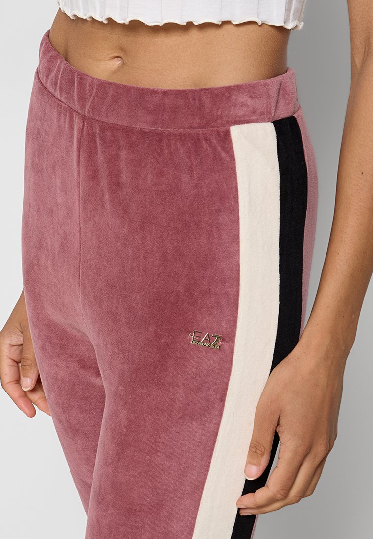 Welurowe dresy w kolorze przykurzonego różu z kremowymi i czarnymi paskami po bokach. Posiadają elastyczny pasek w talii oraz mały metaliczny detal z logo.