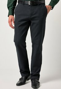 Pantaloni grigi scuri realizzati in tessuto testurizzato, con un design a gamba dritta, tasche laterali, abbinati a scarpe nere e una cintura coordinata.