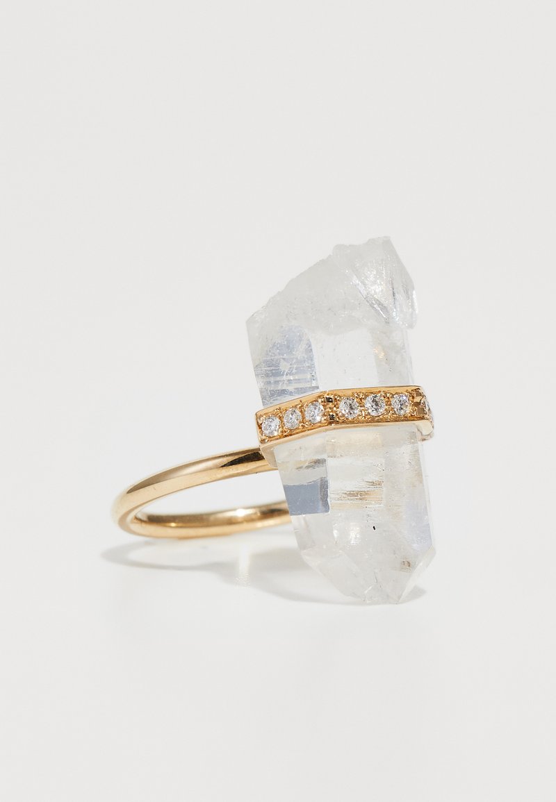 Kristāla gredzens ar caurspīdīgu kvarca kristālu un zelta joslu, ko rotā horizontāla rinda ar maziem caurspīdīgiem dārgakmeņiem.