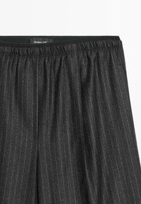 Graue gestreifte Hose mit elastischem Bund. Der Stoff wirkt weich mit feiner Textur. Das Etikett befindet sich oben in der Mitte.