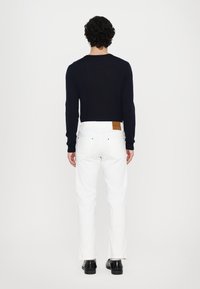 Navy sweater and white jeans viewed from the back. Sweater has a crew neckline; jeans have a tan leather patch on the back waist. Black shoes.
