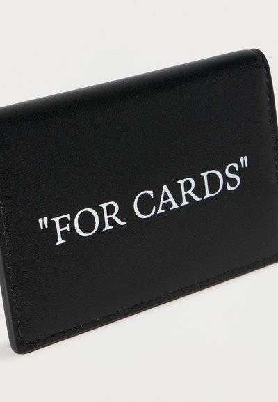 Porte-cartes en cuir noir avec le texte blanc "FOR CARDS" imprimé à l'avant, incliné sur un fond clair uni.