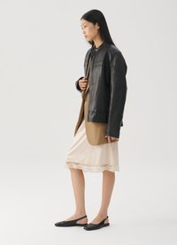 Veste en cuir noir sur un blazer beige, portée avec une robe nuisette rose pâle ornée de dentelle, accompagnée de ballerines à talons slingback noires.