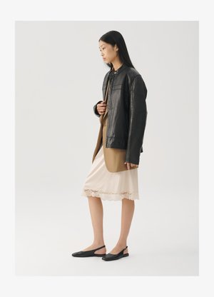 Jachetă neagră de piele peste un top maro, asortată cu o rochie slip de culoare crem deschis, cu dantelă la margini, și pantofi slingback negri.